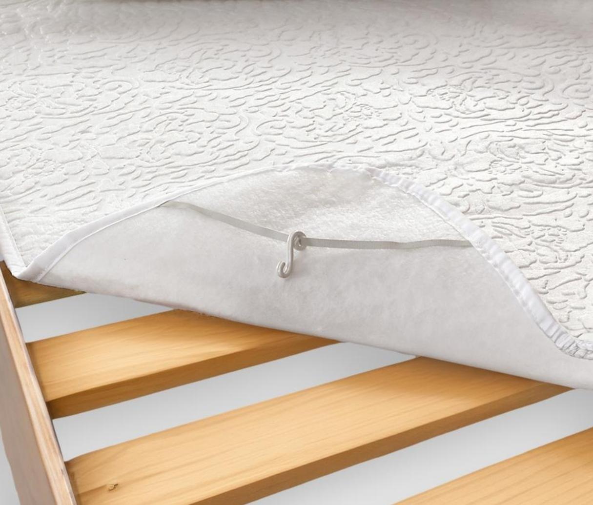 Coprirete bianco con elastico e gancio su un letto con doghe in legno